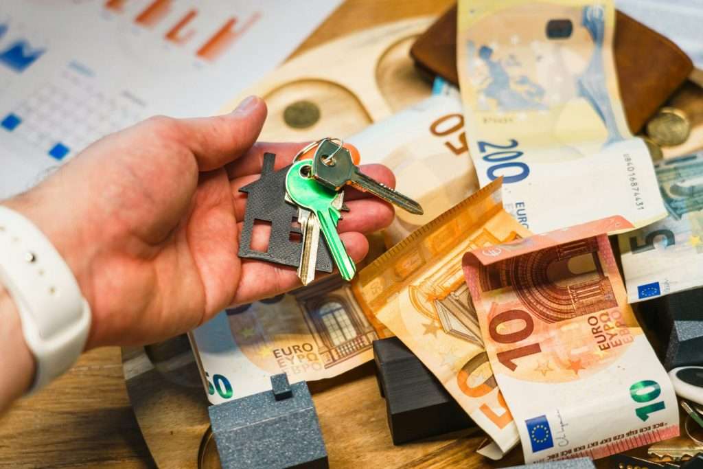 Hand holding house keys over euro banknotes and charts.