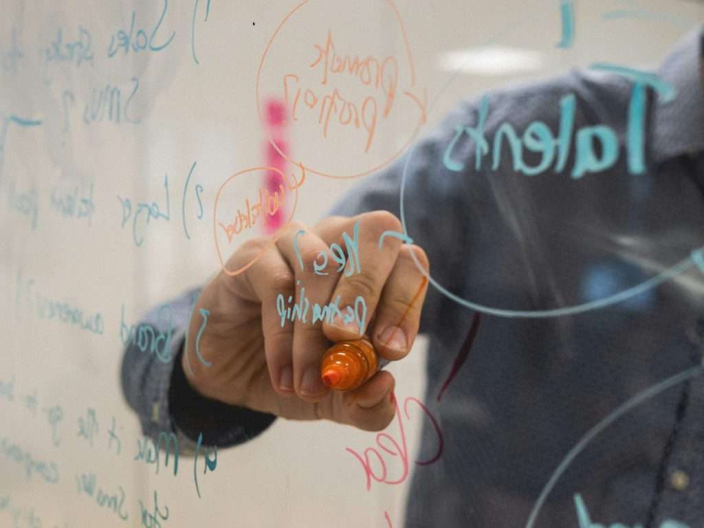 Person writing keyword research diagrams on a glass whiteboard